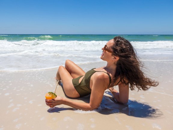 Woman laying in the sand with a cocktail on the beach in Gulf Shores