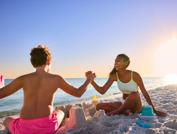 Teens high fiving while building sandcastles on the beach in Gulf Shores
