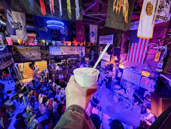 Hand holding a cold bushwacker cocktail while watching live music at Flora-Bama