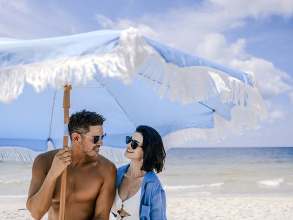 Couple under blue beach umbrella along the shoreline in Gulf Shores