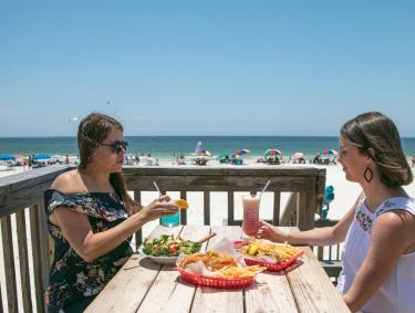 Women enjoying a beachfront meal on the deck at Pink Pony Pub restaurant in Gulf Shores
