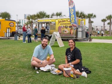 Couple sitting on the green lawn at Gulf Place during the Coastal Alabama Food Truck Festival in Gulf Shores