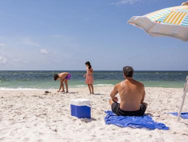 Dad sitting an umbrella on the beach watching his kids play near the shore