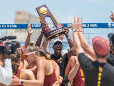 Coach and team celebrating win at NCAA Beach Volleyball Championship in Gulf Shores