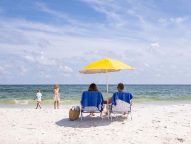 Parents sitting under a beach umbrella watching their kids walk along the shore in Gulf Shores