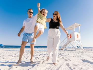 Parents swinging little girl on the beach near a lifeguard stand in Orange Beach