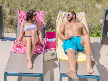 Couple lounging on chairs with cocktails by the pool at The Lodge