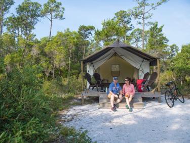 Couple sitting on the front deck area of a rustic tent at The Outpost in Gulf State Park