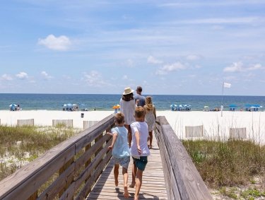 Family walking on a beach boardwalk towards the shore in Orange Beach