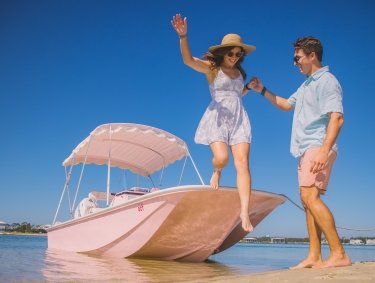 couple stepping onto Robinson Island from a bright pink boat rental in Orange Beach