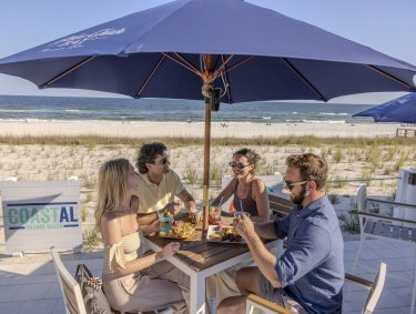 Friends dining under an umbrella at Coastal beachfront restaurant in Orange Beach
