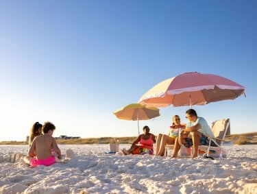 Family relaxing on the beach under an umbrella in Gulf Shores