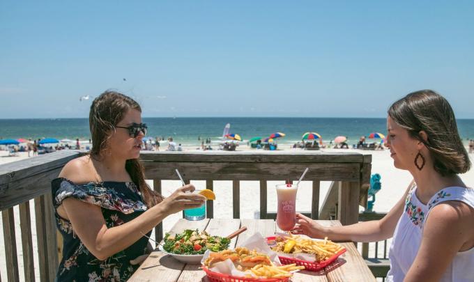 Women enjoying a beachfront meal on the deck at Pink Pony Pub restaurant in Gulf Shores