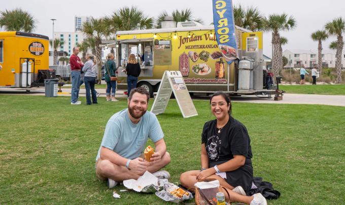 Couple sitting on the green lawn at Gulf Place during the Coastal Alabama Food Truck Festival in Gulf Shores