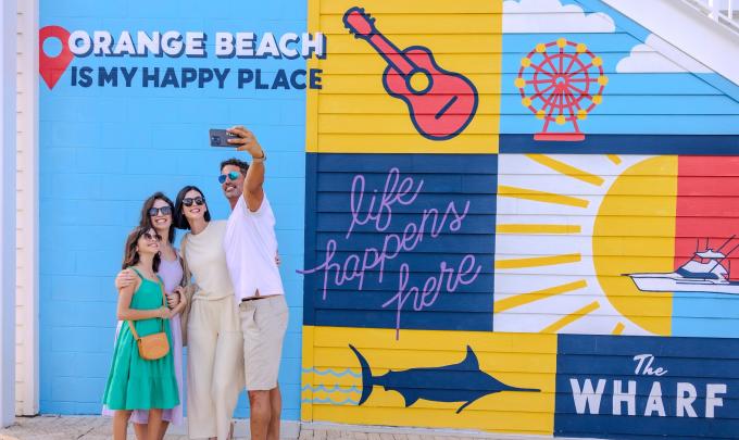 Family taking a selfie in front the mural at The Wharf entertainment district in Orange Beach
