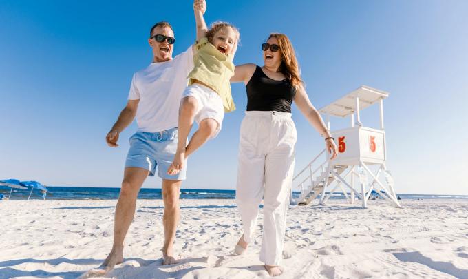 Parents swinging little girl on the beach near a lifeguard stand in Orange Beach