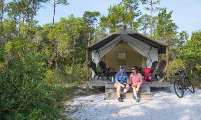 Couple sitting on the front deck area of a rustic tent at The Outpost in Gulf State Park