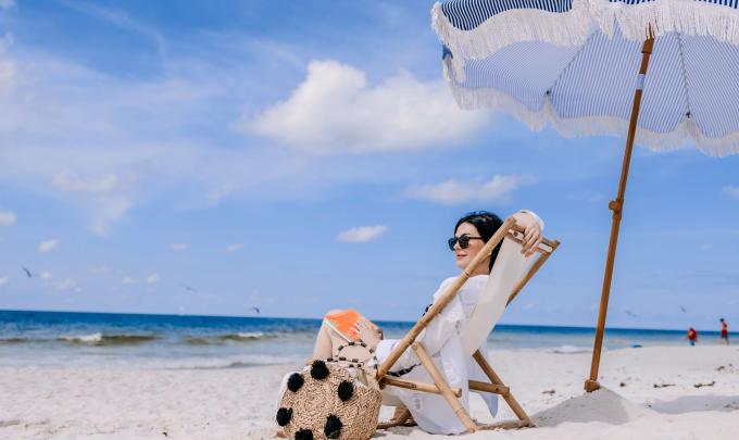 woman relaxing on the beach in a chair under an umbrella looking at the shore