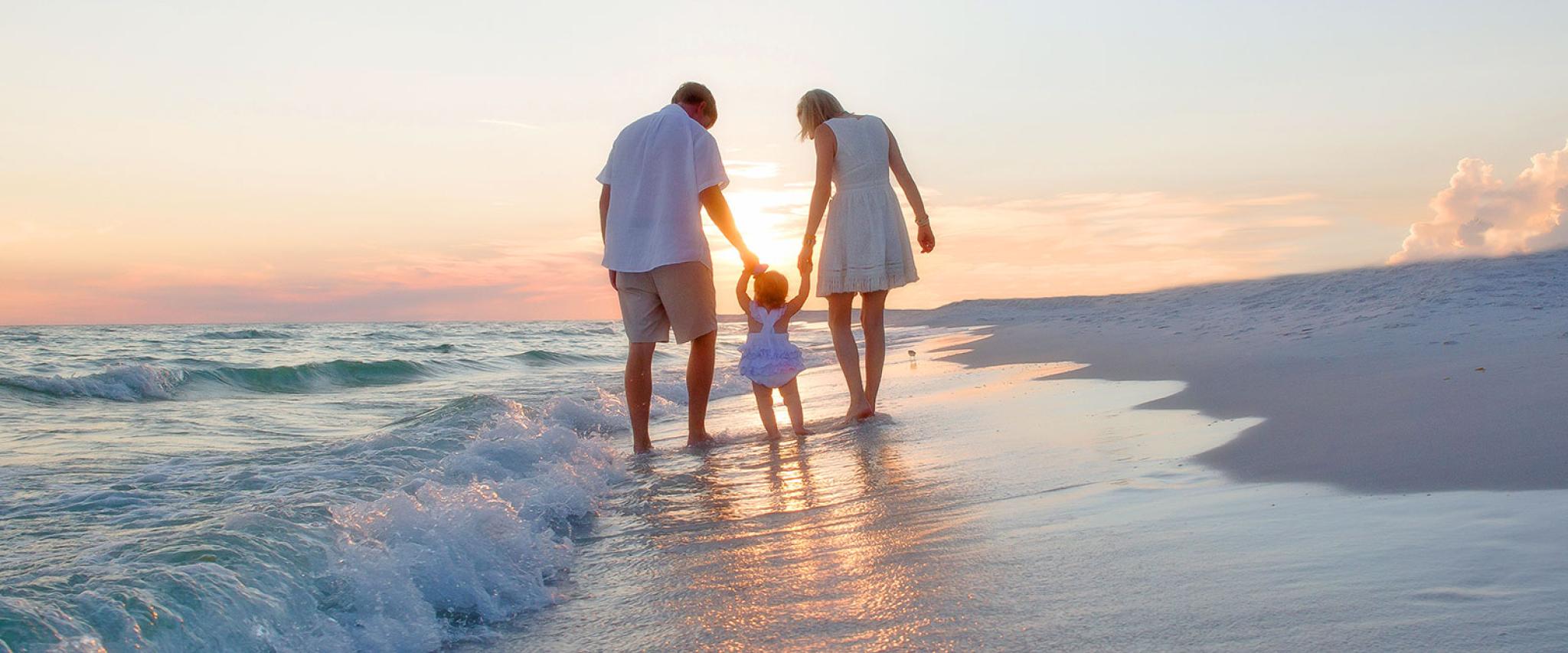 Young Family walks along Alabama's white sand beaches at sunset