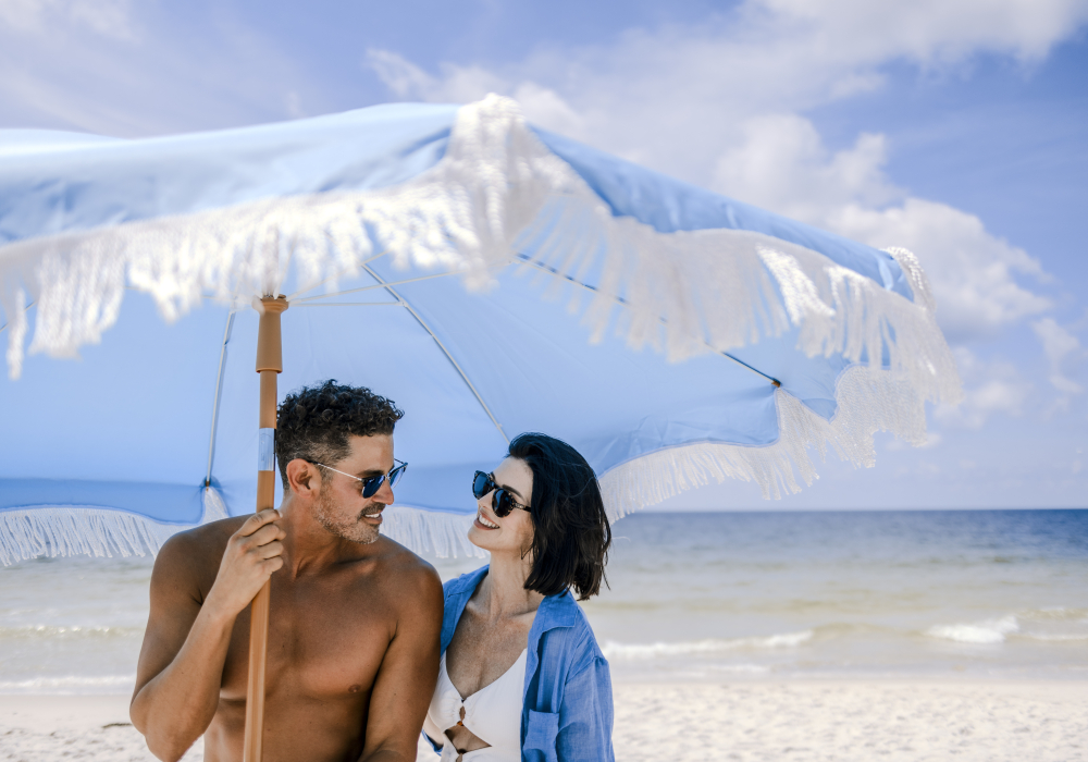 Couple under blue beach umbrella along the shoreline in Gulf Shores