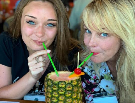 two women sipping a drink from a pineapple orange beach