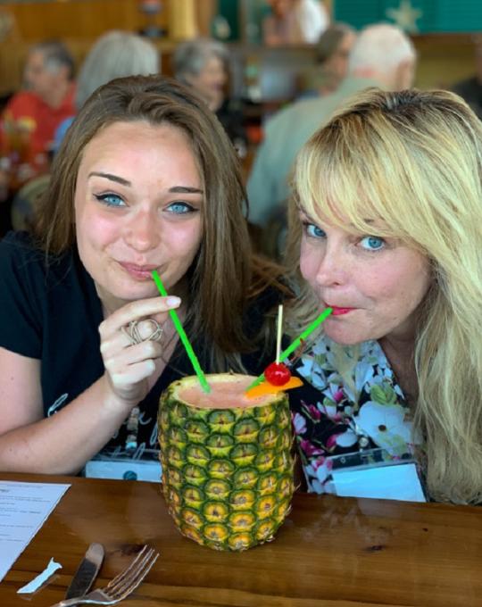 two women sipping a drink from a pineapple orange beach