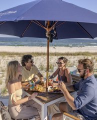 Friends dining under an umbrella at Coastal beachfront restaurant in Orange Beach