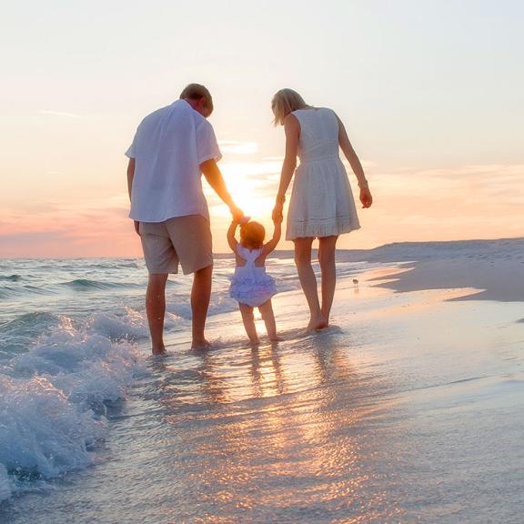 Young Family walks along Alabama's white sand beaches at sunset