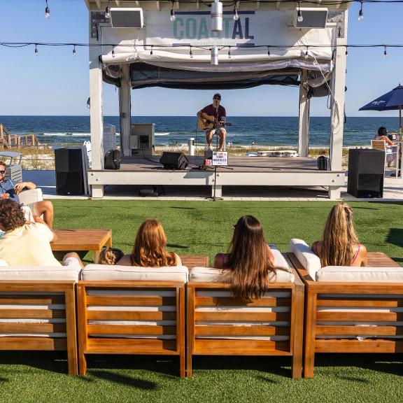 People sitting on couches and listening to live music outdoors at Coastal beachfront restaurant