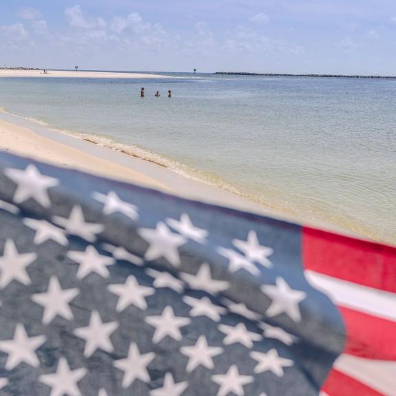 American flag waving in the sand on the beach as children play in the Gulf