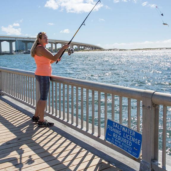 Woman shore fishing into the Gulf at the Perdido Pass seawall in Orange Beach