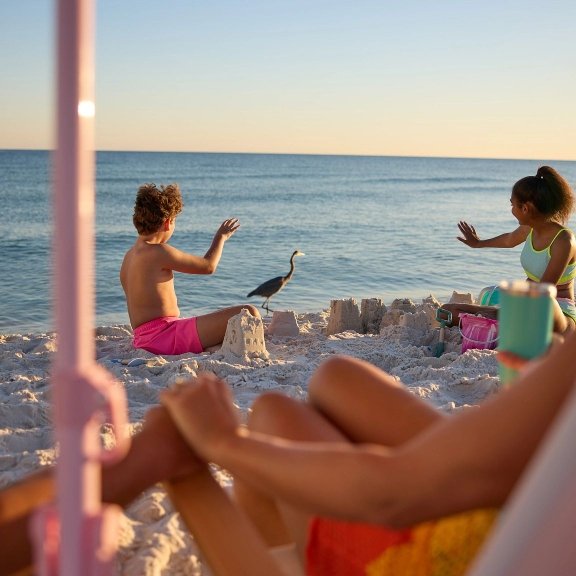 Parents watching kids build sandcastle by the shore on Alabama's Beaches