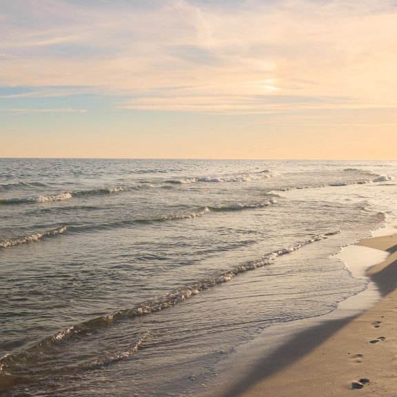 Couple holding hands and walking along the shoreline at sunset in Gulf Shores