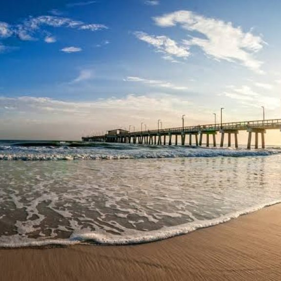 Gulf Shores pier at sunrise with waves washing onto the white sand beach.