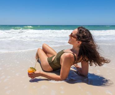 Woman laying in the sand with a cocktail on the beach in Gulf Shores