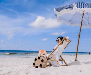 woman relaxing on the beach in a chair under an umbrella looking at the shore