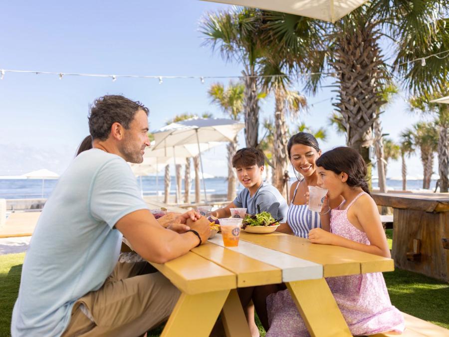 Family dining around a beachfront picnic table at The Gulf seafood restaurant in Orange Beach