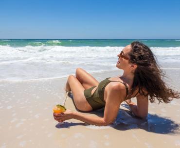 Woman lounging on the beach with a drink in hand in Gulf Shores