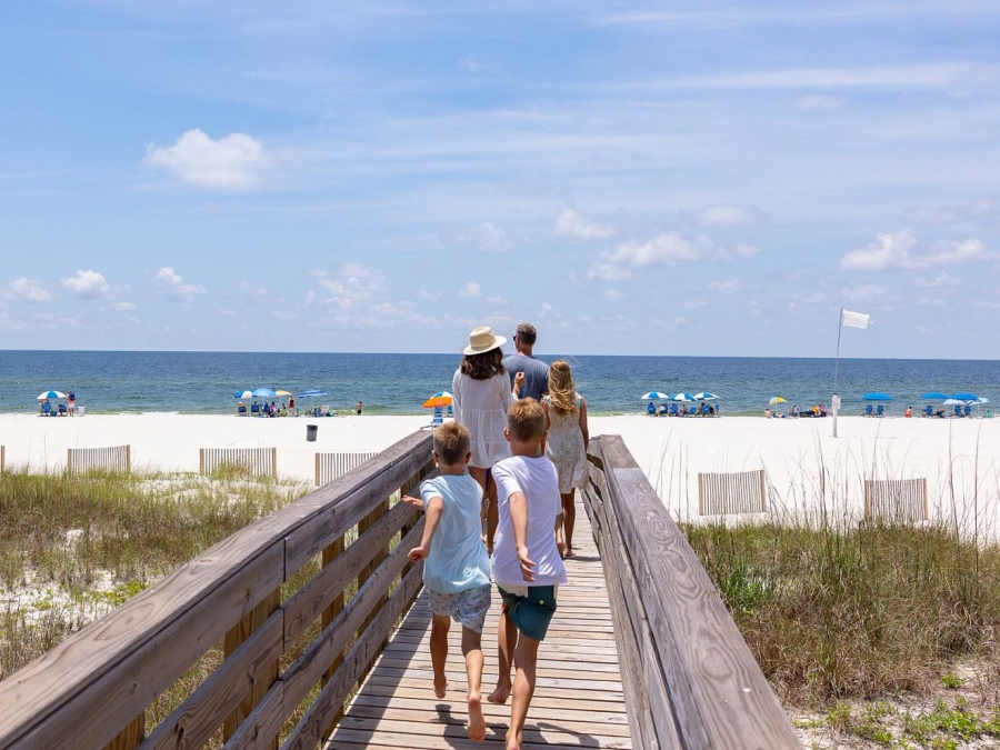 Family walking on a beach boardwalk towards the shore in Orange Beach