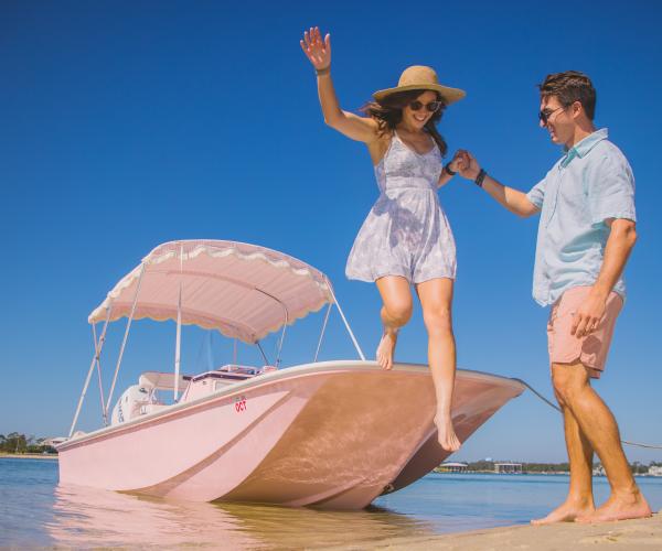 couple stepping onto Robinson Island from a bright pink boat rental in Orange Beach