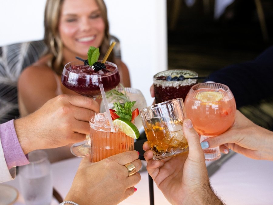 Friends cheersing their glasses together while sitting at a table at Voyage's fine dining restaurant in Orange beach