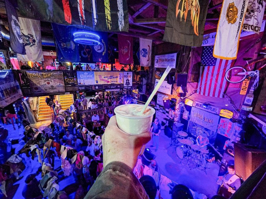 Hand holding a cold bushwacker cocktail while watching live music at Flora-Bama