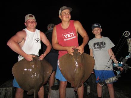 A group of excited kids and teenagers enjoying a thrilling night bowfishing adventure on the Alabama beaches, aiming at a stingray in the shallow water
