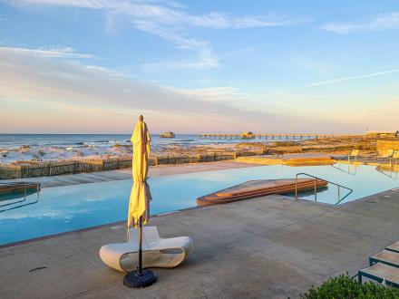 Gulf-front condo rentals at The Lodge at Gulf State Park in Alabama, featuring a pool with Gulf views and a nearby pier at sunset