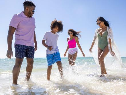A young family of four plays in the waves along Alabama’s Beaches