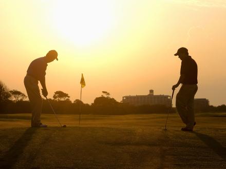 Two people playing golf at sunset
