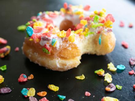 Cake donut topped with glaze and Fruity Pebbles cereal