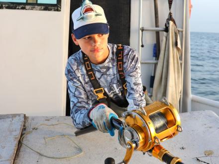 Boy holding a fishing reel on a shark fishing charter boat in Orange Beach