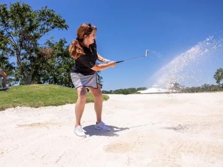 Women hitting a ball out of a sand bunker at Craft Farms golf course in Gulf Shores