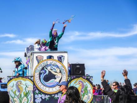 Woman throwing beads off a float during a Mardi Gras parade